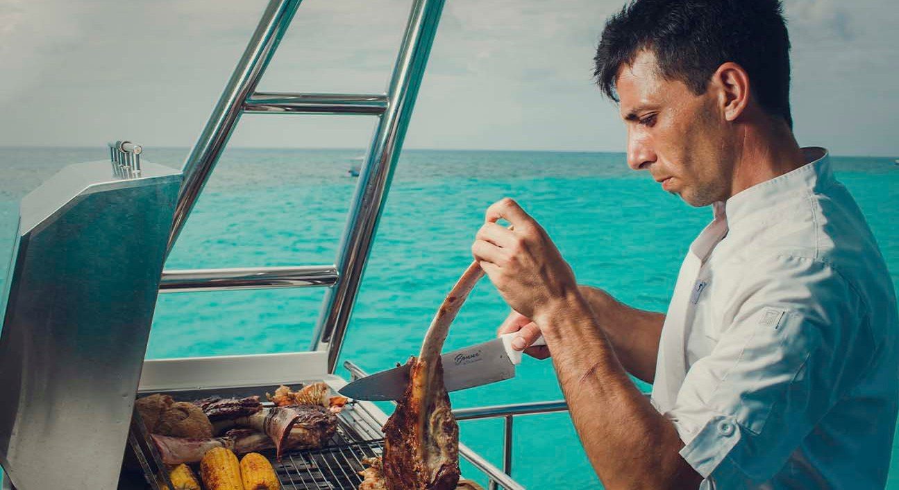 Private chef grilling tomahawk steak onboard over turquoise water